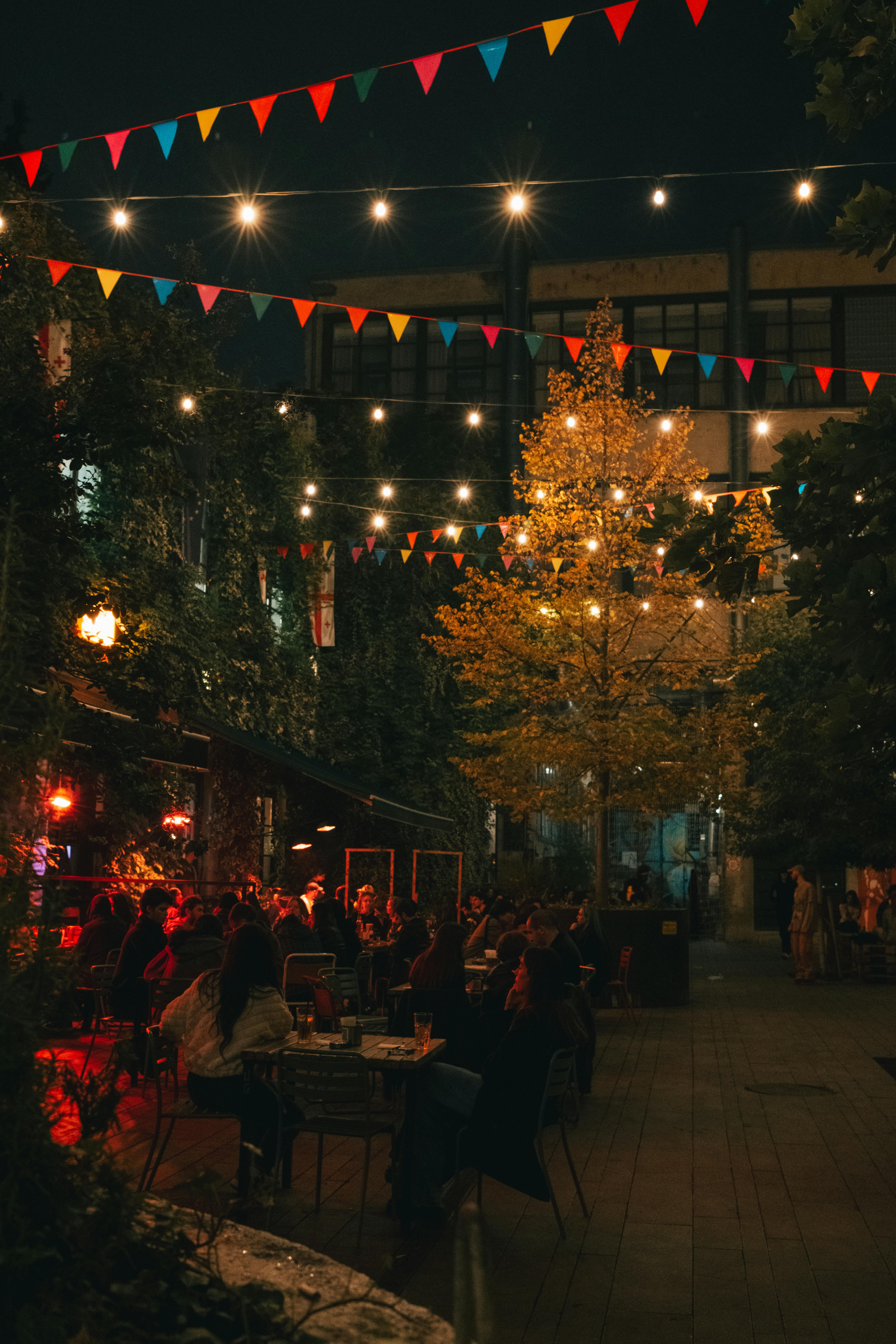 Outdoor tables with lights and people eating in the evening
